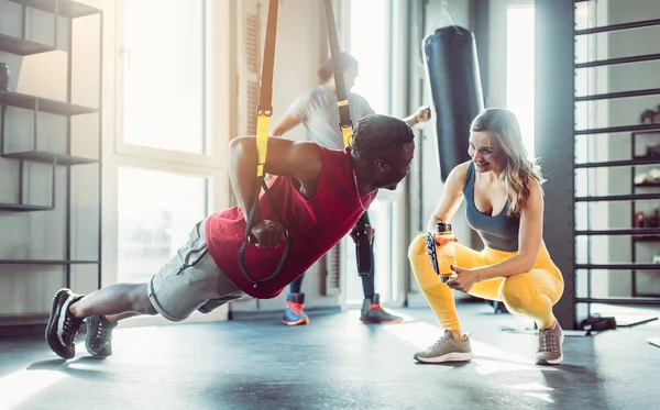 Woman and man at sling trainer in gym during workout
