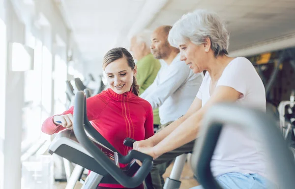 健身教练在健身房帮助老年人进行有氧自行车训练 — 图库照片