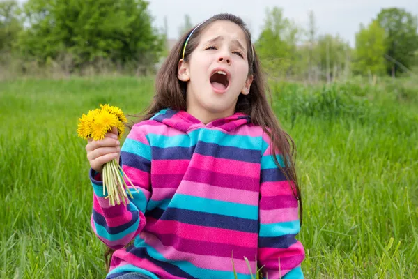 Sneezing girl on meadow with dandelions — Stock Photo, Image