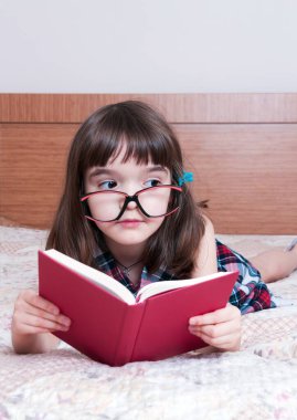 Evde kitap okuyan küçük bir kız.