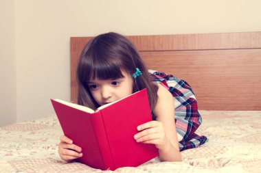 Evde kitap okuyan küçük bir kız.