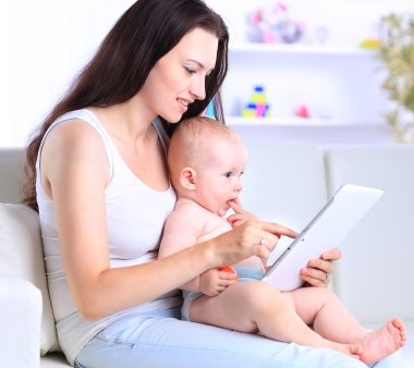 Anne ve bebek evdeki kanepede oyun oynayıp tablet bilgisayar okumak istiyorlar.