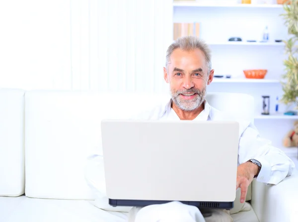 Senior man i soffa med bärbar dator — Stockfoto