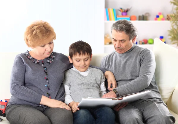 Ragazzo carino seduto in grembo ai loro nonni e guardando felicemente insieme a una foto — Foto Stock