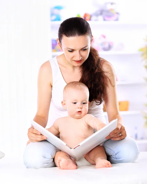 Encantadora madre mostrando imágenes en un libro a su pequeño y lindo hijo en casa — Foto de Stock