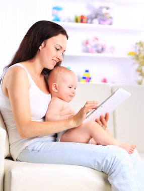 Anne ve bebek evdeki kanepede oyun oynayıp tablet bilgisayar okumak istiyorlar.