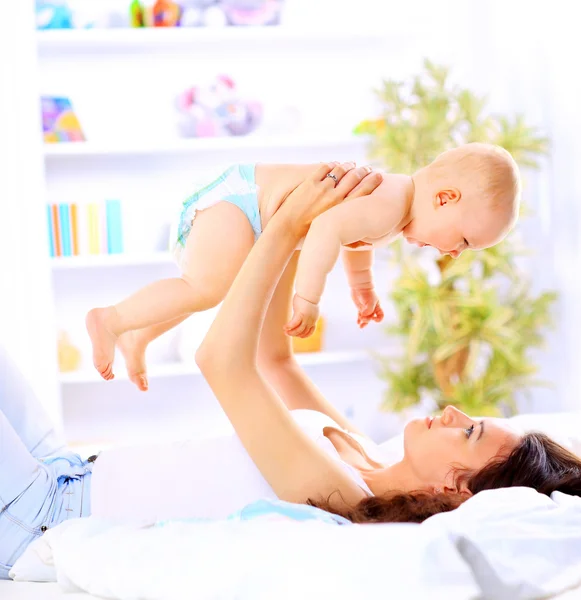 Happy beautiful young mother and baby laying on sofa — Stock Photo, Image