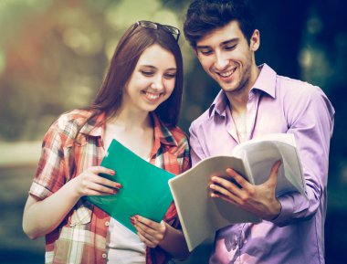 güneşli bir parkta kitaplarla mutlu öğrenci grubu.