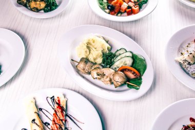 Barbekülü patates püresi, taze sebze salatası ve masada diğer yemekler.
