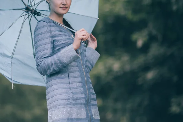 Молодая женщина с зонтиком стоит на дорожке в парке. — стоковое фото