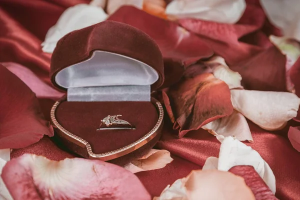 Diamond ring en rose bloemblaadjes op heldere rode achtergrond — Stockfoto