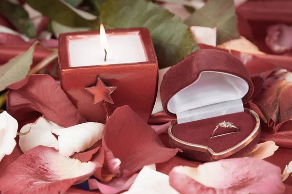 玫瑰花瓣背景上的蜡烛和钻石戒指 — 图库照片