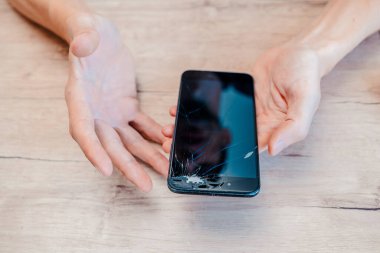 Genç bir adamın ellerinde kırık bir ekranla akıllı telefon..
