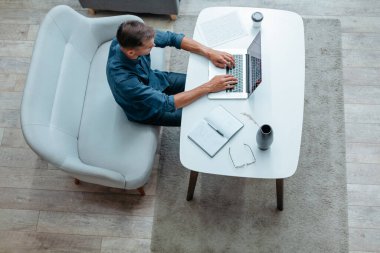 Genç adam evinde dizüstü bilgisayarla çalışıyor..