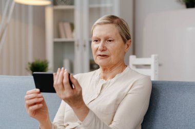 Kanepede oturan akıllı telefonlu olgun bir kadın..