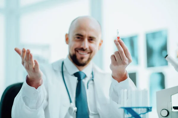 Científico feliz con una ampolla de vacuna sentada en la mesa de laboratorio . — Foto de Stock