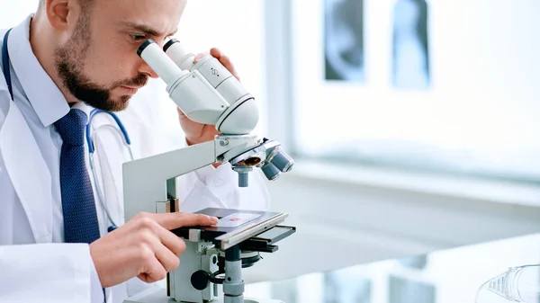 Cientista olhando através de um microscópio sentado em uma mesa de laboratório. — Fotografia de Stock