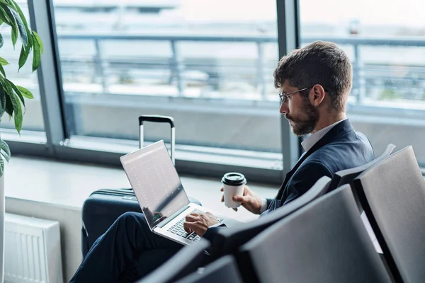Homem com um café takeaway usando um laptop no aeroporto departu — Fotografia de Stock
