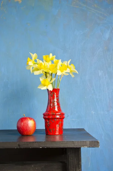 Yellow narcissus in red vase and apple — Stock Photo, Image
