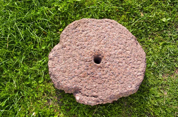 Old cracked millstone on grass — Stock Photo, Image