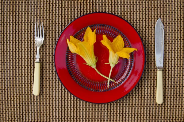 Twee zomerbloemen pompoen courgette in rode plaat op tafel — Stockfoto