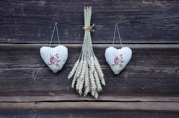 Dos corazones de tela símbolos y espigas de trigo manojo en la pared — Foto de Stock