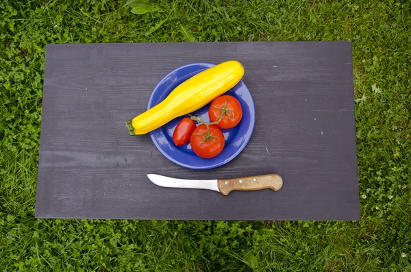 在蓝色的盘子，在花园里的黑桌子上的蔬菜 — 图库照片