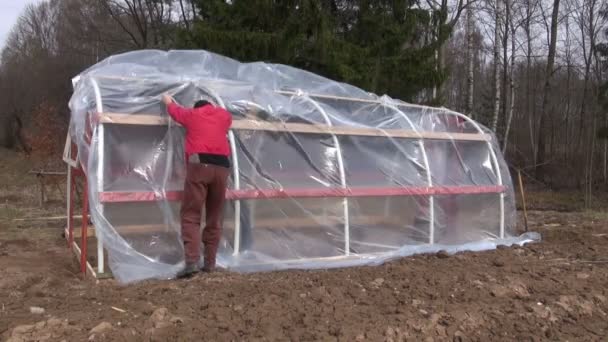 Рабочие на весенней ферме делают новую пластиковую теплицу — стоковое видео