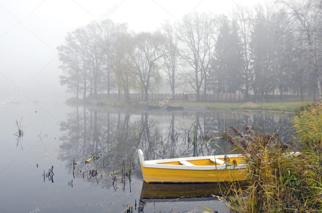 yellow wooden boat on autumn lake and morning mist
