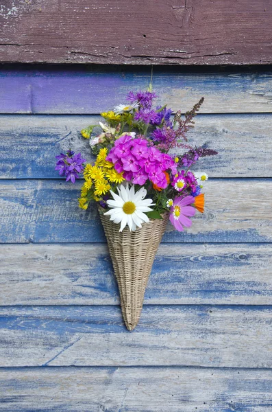 Красивые цветы в плетеной корзине на старой деревянной стене — стоковое фото