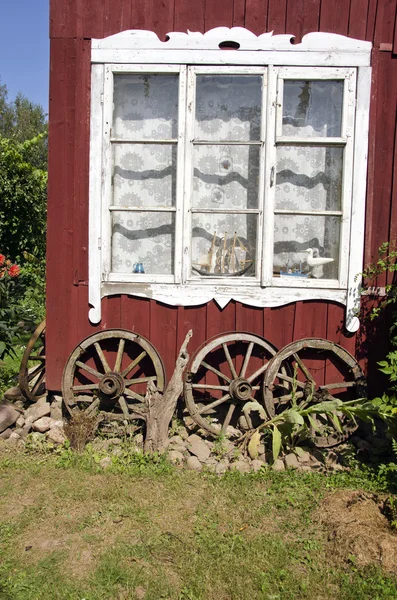 Village house old window with ancient horse carriage wheel — Stock Photo, Image