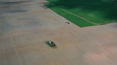 Traktör, sonbaharda tarım arazisindeki küçük yalnız şapelin yanında mahsul ekiyor, hava manzarası...