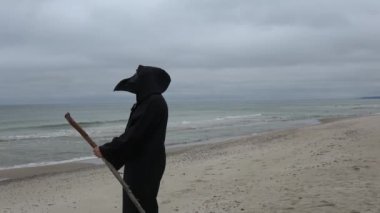 Elinde sopayla denize bakan siyah maskeli bir plaket doktoru. Tüm salgınların resmi