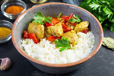 Baharatlı körili tavuk ve pilav. Koyu arkaplanda tavuk ve pilav ile köri sosu.