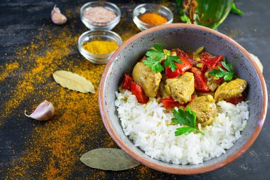 Baharatlı körili tavuk ve pilav. Koyu arkaplanda tavuk ve pilav ile köri sosu.