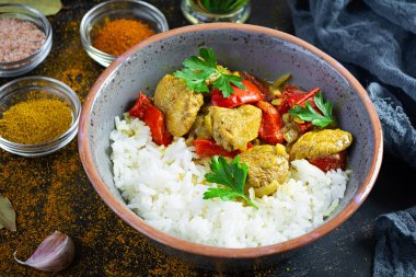 Baharatlı körili tavuk ve pilav. Koyu arkaplanda tavuk ve pilav ile köri sosu.