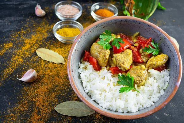 Baharatlı körili tavuk ve pilav. Koyu arkaplanda tavuk ve pilav ile köri sosu.