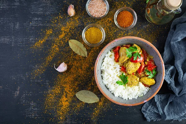 Baharatlı körili tavuk ve pilav. Koyu arkaplanda tavuk ve pilav ile köri sosu. Üst görünüm