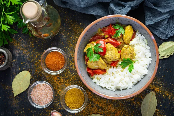 Baharatlı körili tavuk ve pilav. Koyu arkaplanda tavuk ve pilav ile köri sosu. Üst görünüm
