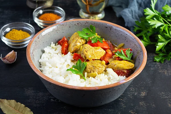 Baharatlı körili tavuk ve pilav. Koyu arkaplanda tavuk ve pilav ile köri sosu.