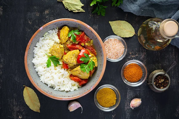 Baharatlı körili tavuk ve pilav. Koyu arkaplanda tavuk ve pilav ile köri sosu. Üst görünüm