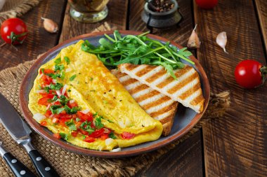 Fried omelette with tomatoes, onion and herbs. Delicious breakfast with eggs and toasts