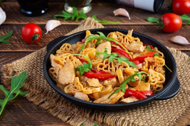 Tasty pasta in tomato sauce with chicken, pepper and herbs on wooden background