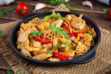 Tasty pasta in tomato sauce with chicken, pepper and herbs on wooden background