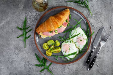 Kızarmış yumurtalı kahvaltı ve jambonlu kruvasan sandviçi, peynir ve salata. Lezzetli sabah kahvaltısı. Üst görünüm