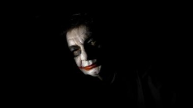Bloody Halloween theme. An evil joker. Painted spooky joker face against black background.