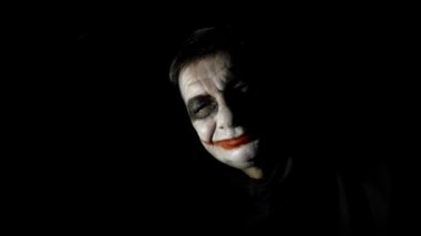 Bloody Halloween theme. An evil joker. Painted spooky joker face against black background.
