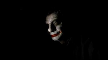 Bloody Halloween theme. An evil joker. Painted spooky joker face against black background.