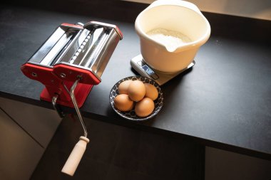 Makarna makinesi ve malzemeler mutfak masasında.