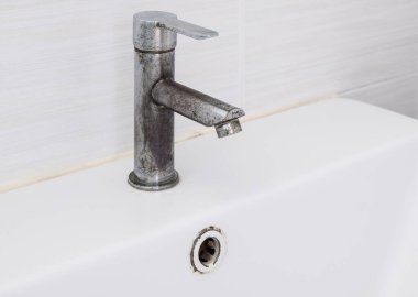 Seramik lavabo lavabosu. Lekeli musluk şehir evindeki tuvaletin beyaz fayans duvarının yanında. Arka plan için ön manzara..